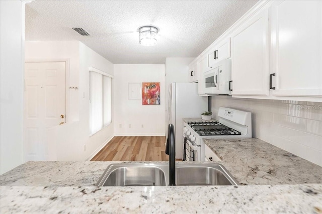 kitchen featuring white cabinets, light wood-type flooring, white appliances, and light stone countertops