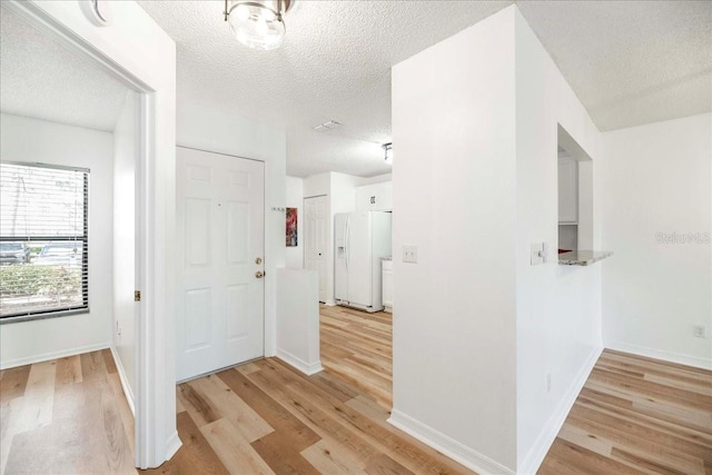 hallway with light hardwood / wood-style floors and a textured ceiling