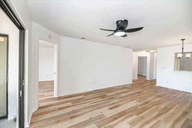 unfurnished living room featuring ceiling fan with notable chandelier, light hardwood / wood-style floors, and a textured ceiling