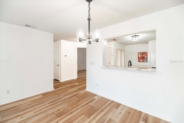 unfurnished room featuring light hardwood / wood-style flooring, a chandelier, a textured ceiling, and sink