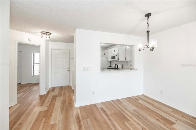 unfurnished dining area featuring a textured ceiling, light hardwood / wood-style floors, an inviting chandelier, and sink