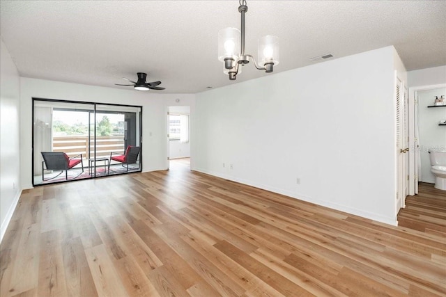 unfurnished living room featuring a textured ceiling, ceiling fan with notable chandelier, and light wood-type flooring