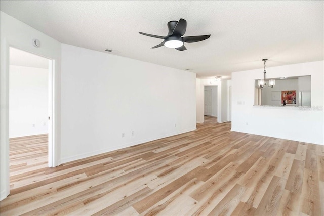 unfurnished living room with ceiling fan with notable chandelier, a textured ceiling, and light hardwood / wood-style flooring