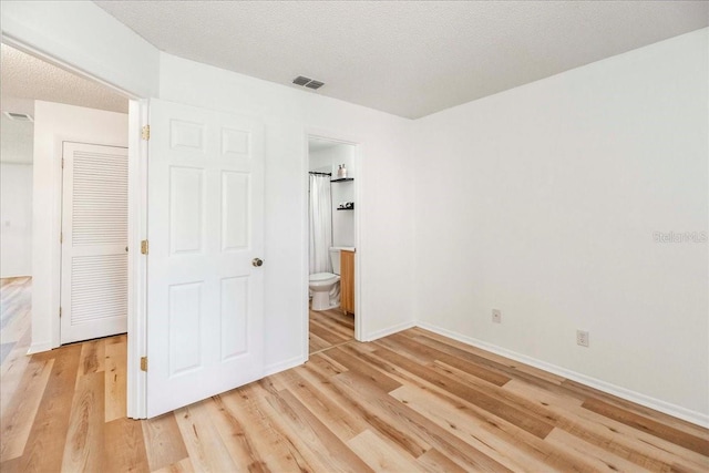 unfurnished bedroom featuring connected bathroom, light hardwood / wood-style floors, and a textured ceiling