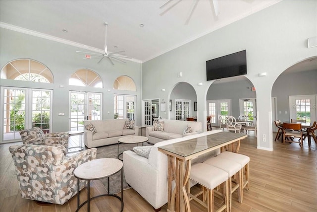 living room featuring french doors, ornamental molding, ceiling fan, a high ceiling, and light hardwood / wood-style floors