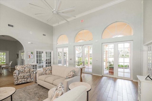 living room with french doors, ornamental molding, ceiling fan, light hardwood / wood-style flooring, and a high ceiling