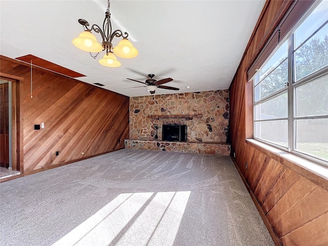 unfurnished living room featuring a fireplace, wood walls, plenty of natural light, and ceiling fan with notable chandelier