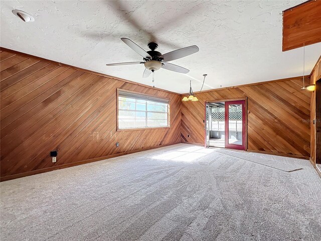 carpeted spare room featuring a textured ceiling, ceiling fan, and wooden walls