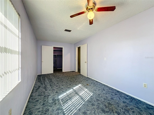 unfurnished bedroom with a textured ceiling, a closet, dark carpet, and ceiling fan