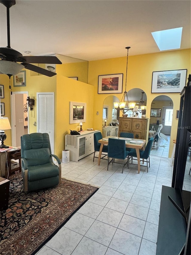 living room featuring light tile patterned floors, ceiling fan with notable chandelier, and lofted ceiling with skylight