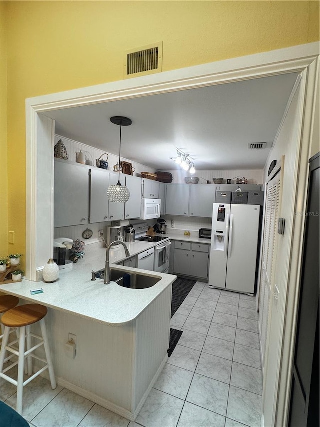 kitchen featuring pendant lighting, white appliances, sink, a kitchen bar, and kitchen peninsula