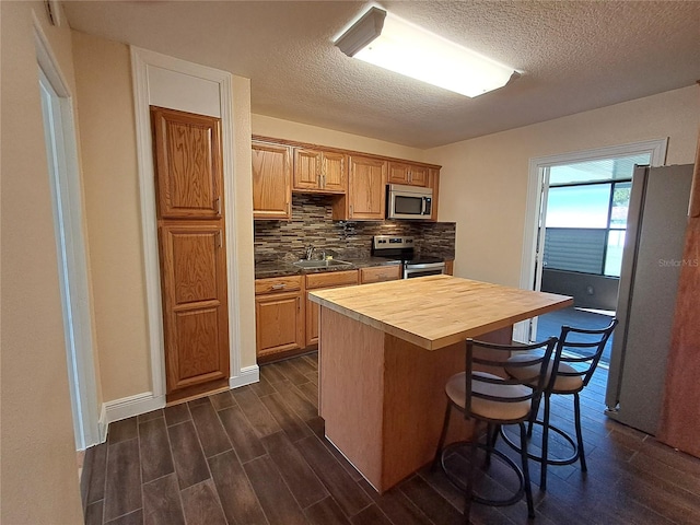 kitchen with appliances with stainless steel finishes, a textured ceiling, sink, dark hardwood / wood-style floors, and butcher block counters