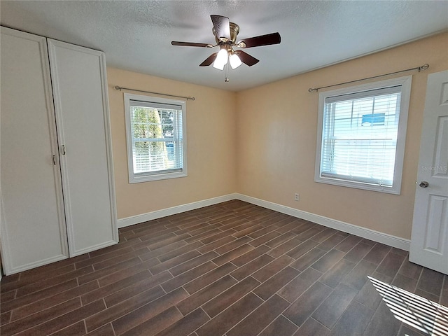 unfurnished bedroom with multiple windows, a textured ceiling, dark hardwood / wood-style floors, and ceiling fan