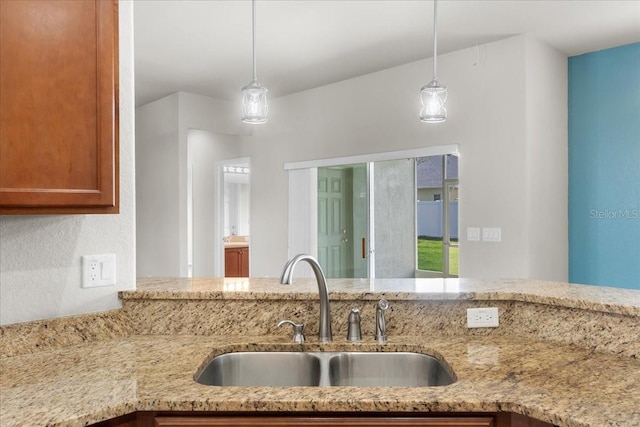 kitchen featuring hanging light fixtures, sink, and light stone counters