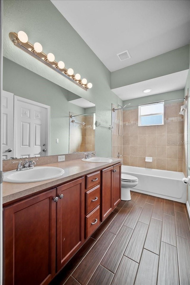 full bathroom with tiled shower / bath, vanity, and toilet