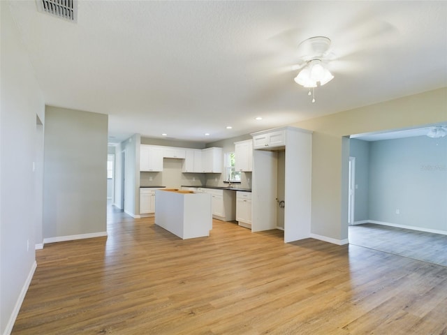 kitchen with white cabinetry, ceiling fan, stainless steel dishwasher, a kitchen island, and light wood-type flooring