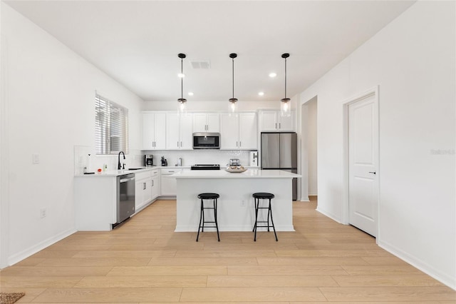 kitchen with a center island, stainless steel appliances, white cabinetry, and hanging light fixtures