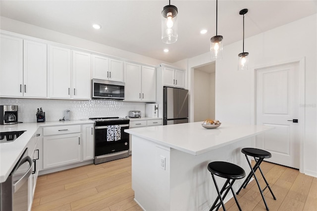 kitchen with stainless steel appliances, white cabinets, a center island, light hardwood / wood-style floors, and hanging light fixtures