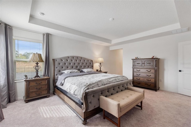 bedroom with a tray ceiling, light carpet, and a textured ceiling