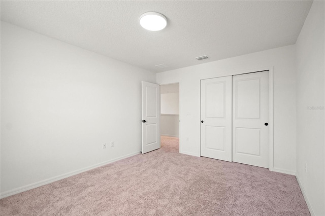 unfurnished bedroom featuring light carpet, a closet, and a textured ceiling