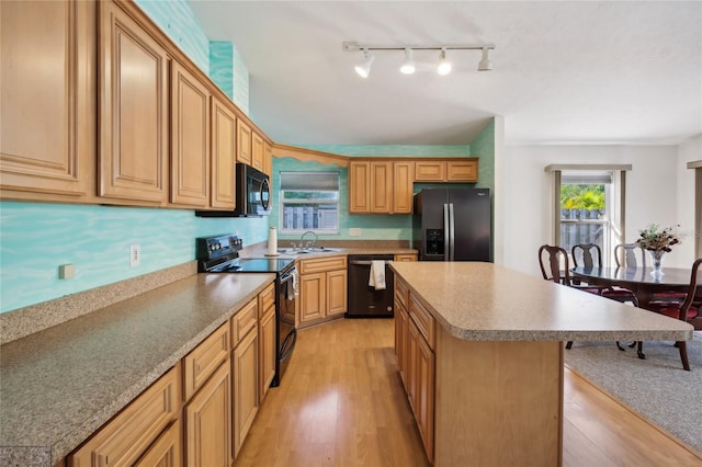 kitchen featuring a kitchen breakfast bar, sink, black appliances, light hardwood / wood-style flooring, and a kitchen island