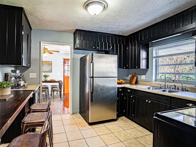 kitchen featuring sink, ceiling fan, light tile patterned floors, a textured ceiling, and stainless steel refrigerator