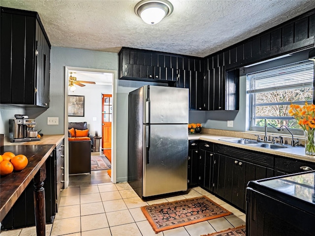 kitchen with a textured ceiling, ceiling fan, sink, light tile patterned floors, and stainless steel refrigerator