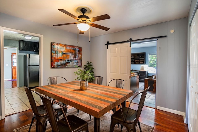 dining space with a barn door, ceiling fan, and dark wood-type flooring