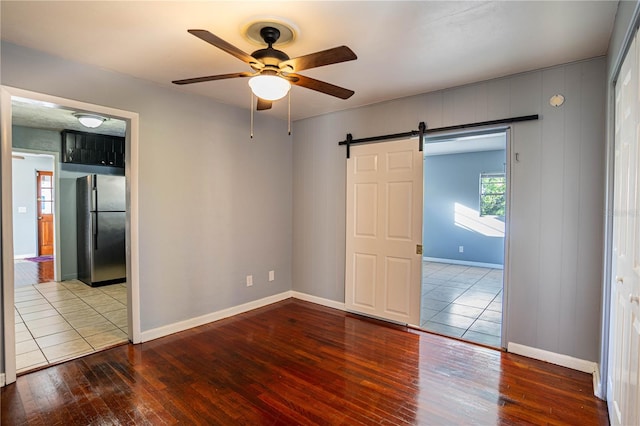 unfurnished room featuring a barn door, hardwood / wood-style flooring, and ceiling fan