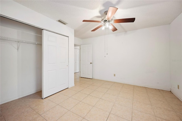 unfurnished bedroom featuring ceiling fan, a closet, light tile patterned flooring, and a textured ceiling