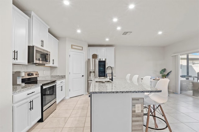 kitchen with white cabinets, a kitchen bar, stainless steel appliances, and an island with sink