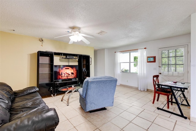 tiled living room featuring ceiling fan, a fireplace, and a textured ceiling