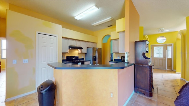 kitchen with light tile patterned floors, kitchen peninsula, stainless steel fridge, and electric range