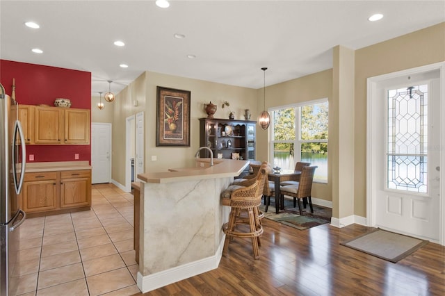 kitchen with stainless steel fridge, a kitchen island with sink, light hardwood / wood-style flooring, hanging light fixtures, and a breakfast bar area