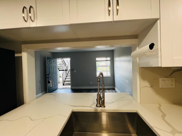 kitchen with light stone counters, white cabinetry, and sink