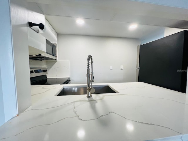 kitchen with stove, tasteful backsplash, stainless steel refrigerator, and sink