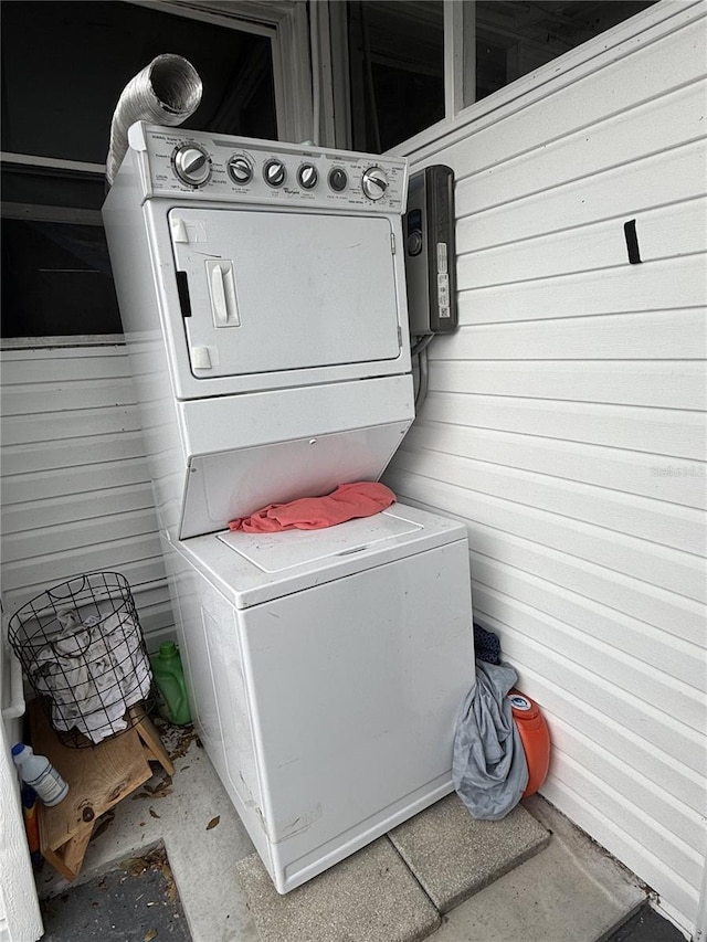 clothes washing area with stacked washer / drying machine and wood walls