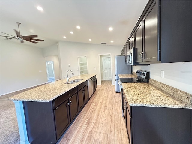 kitchen featuring lofted ceiling, sink, light stone counters, stainless steel appliances, and an island with sink