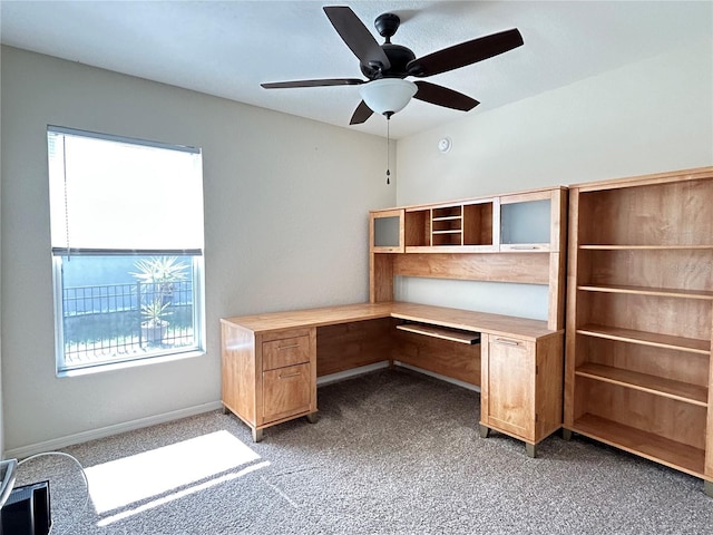 unfurnished office with ceiling fan, built in desk, and light colored carpet