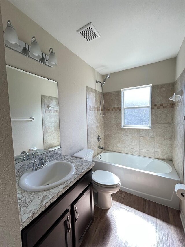 full bathroom with tiled shower / bath combo, toilet, vanity, and hardwood / wood-style floors