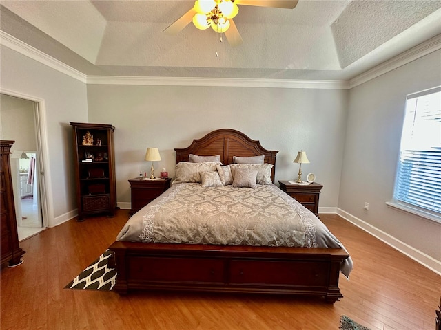 bedroom with a raised ceiling, ceiling fan, wood-type flooring, and ornamental molding