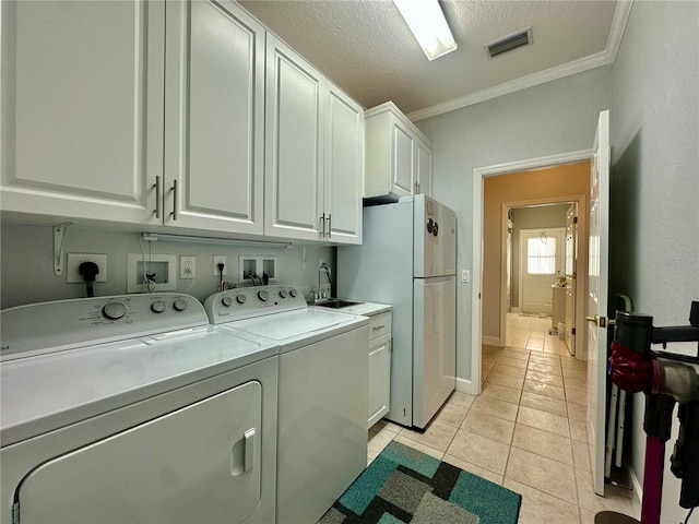 washroom featuring cabinets, a textured ceiling, washer and clothes dryer, light tile patterned floors, and ornamental molding