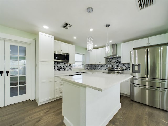 kitchen featuring white cabinets, stainless steel appliances, a center island, and wall chimney range hood