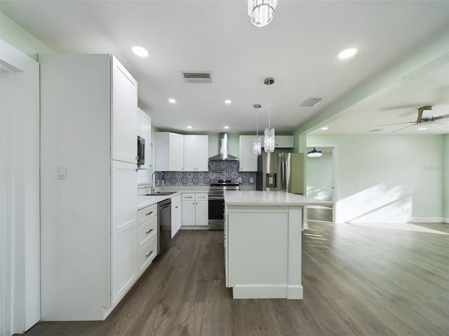 kitchen with sink, decorative light fixtures, wall chimney range hood, stainless steel appliances, and white cabinets