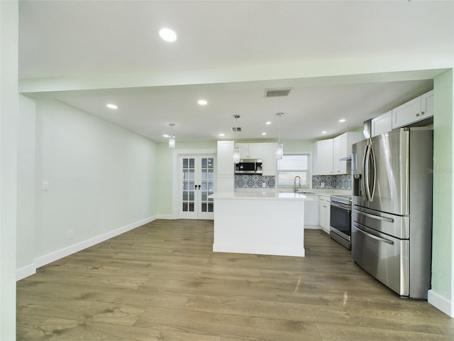 kitchen with stainless steel appliances, a center island, white cabinets, and decorative light fixtures