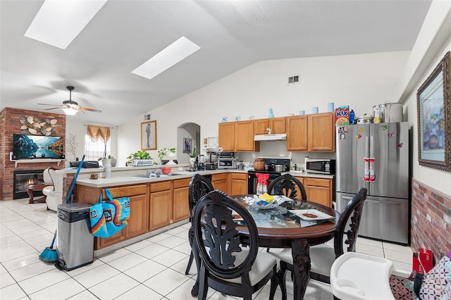 kitchen with appliances with stainless steel finishes, lofted ceiling with skylight, ceiling fan, sink, and light tile patterned floors