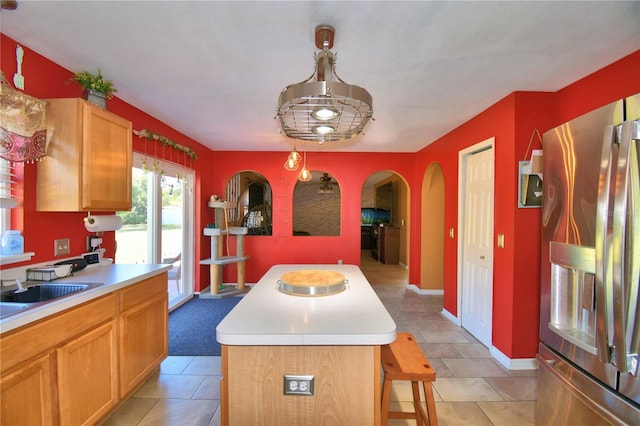 kitchen with stainless steel fridge, a kitchen island, hanging light fixtures, and sink