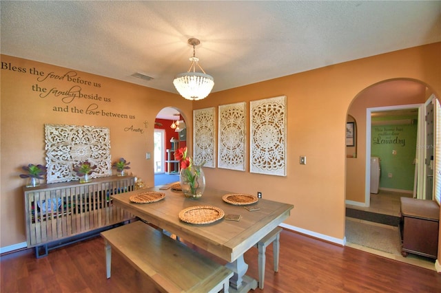 dining area with a textured ceiling, washer / clothes dryer, dark wood-type flooring, and a notable chandelier