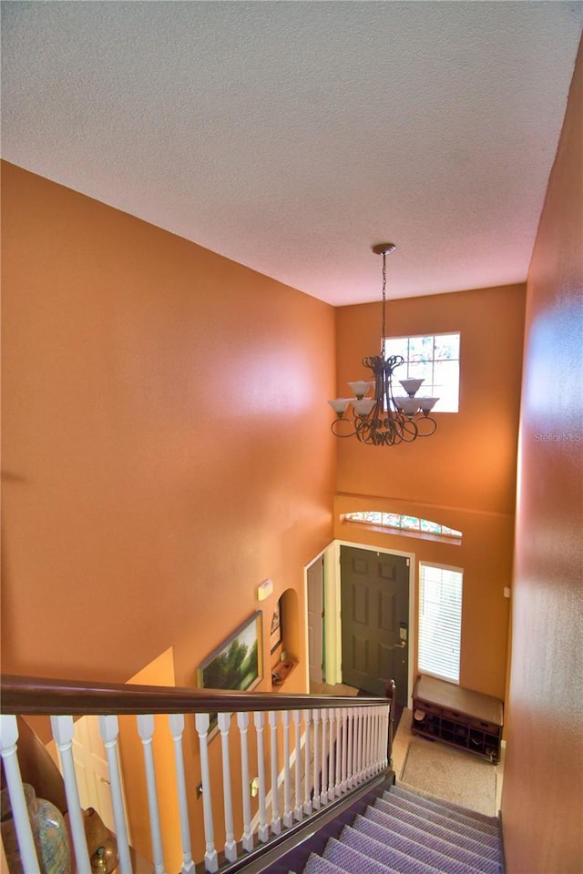 stairway featuring carpet, a textured ceiling, and a notable chandelier