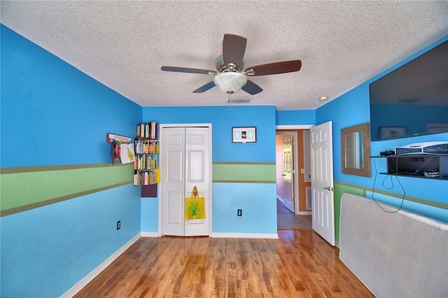 unfurnished bedroom featuring ceiling fan, a closet, a textured ceiling, and hardwood / wood-style flooring